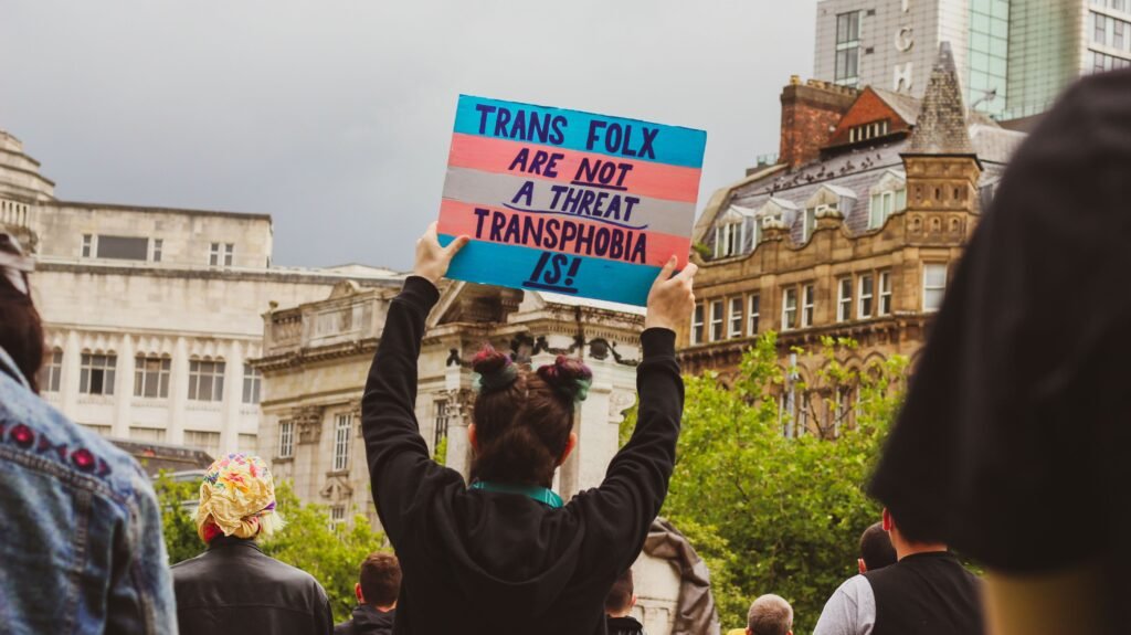 Protest scene with a sign advocating against transphobia in an urban setting.